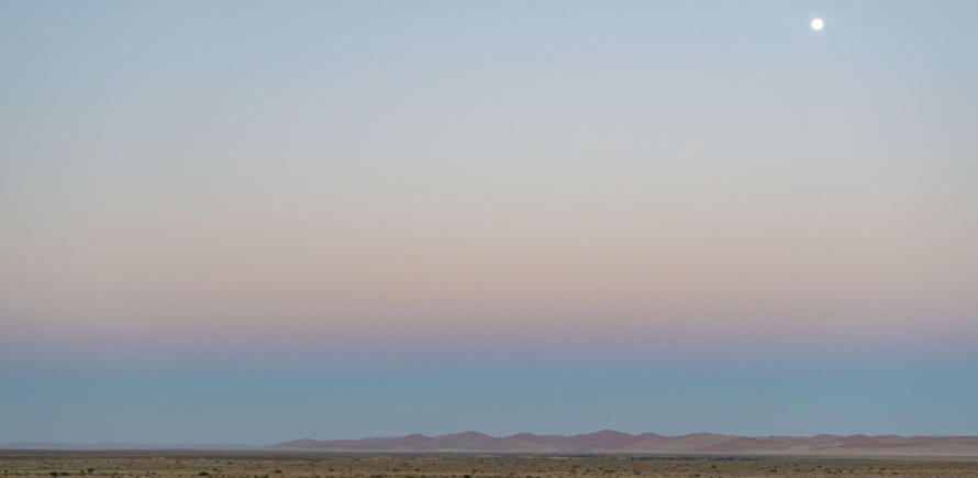 Blick auf die Namib bei Sonnenaufgang mit Vollmond am Himmel