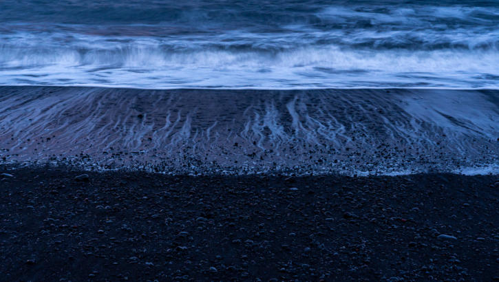 Wellenmuster auf schwarzem Strand